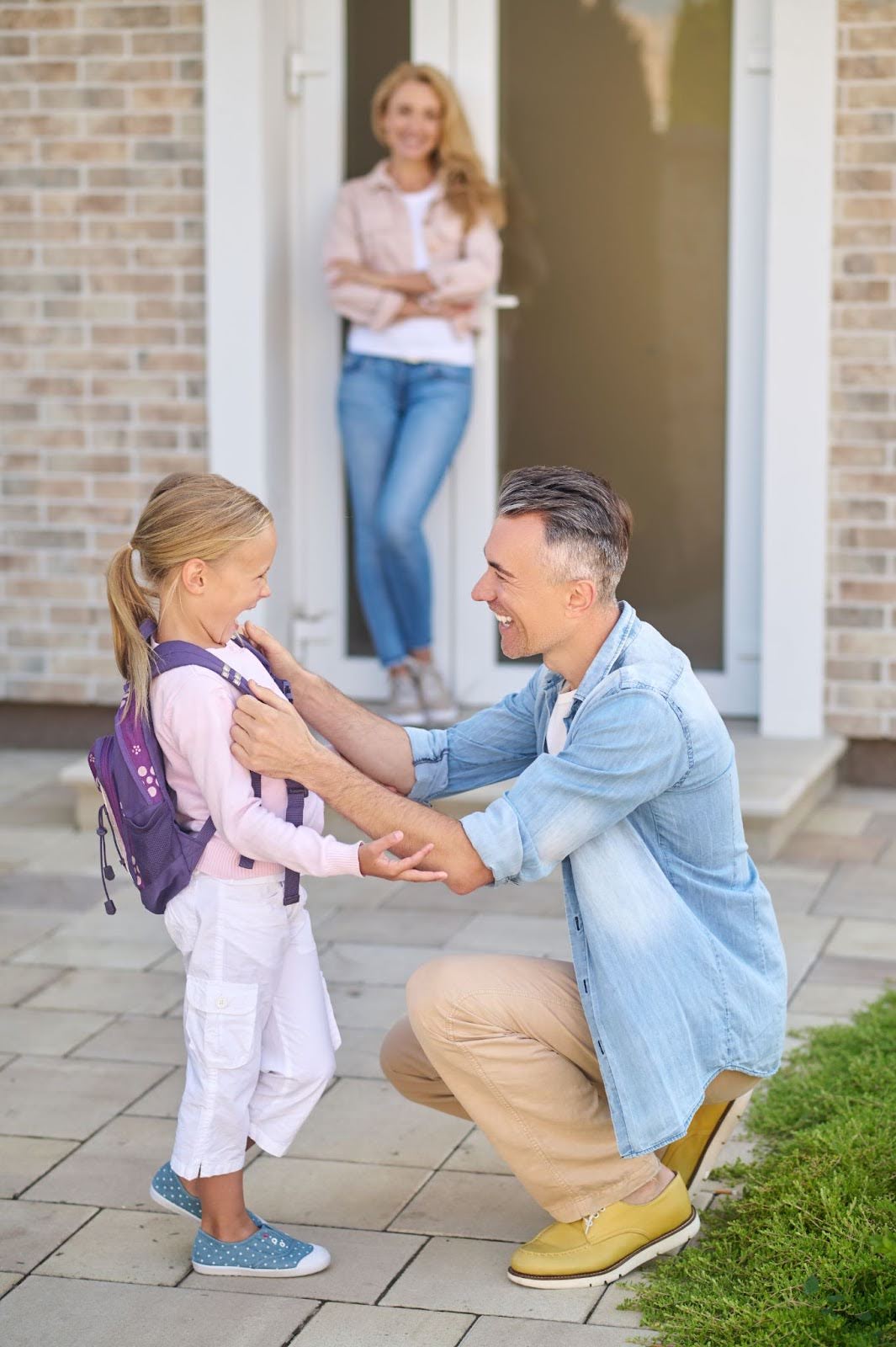 Man helping his daughter get to school with wife standing in the background.