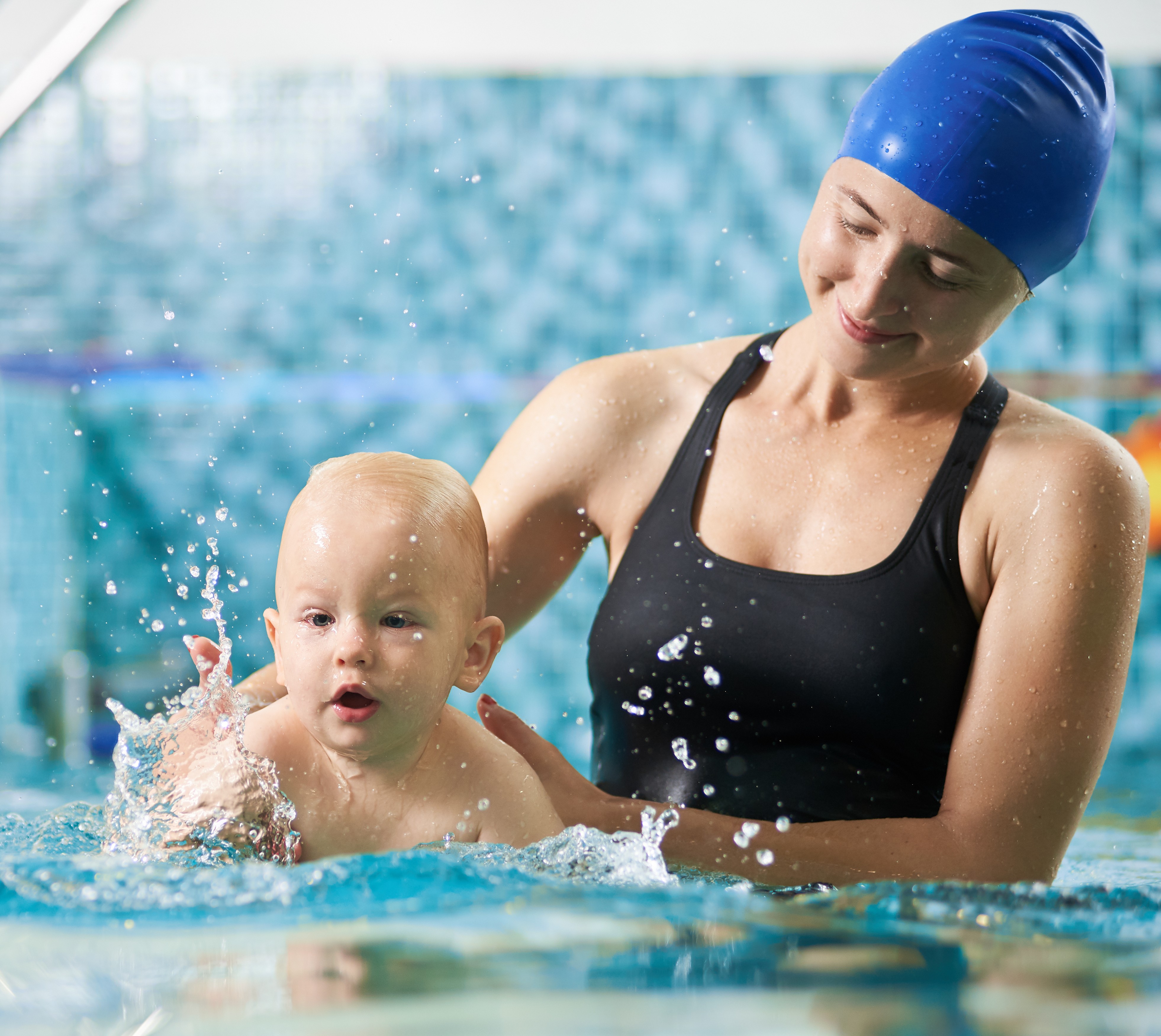 Swimming instructor in pool with baby teaching him how to swim